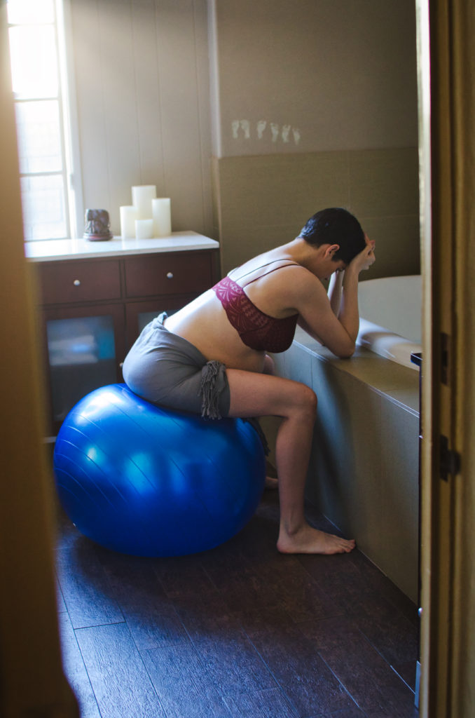 A pregnant woman in labor at babymoon birth center leans on the edge of the tub during a contraction.